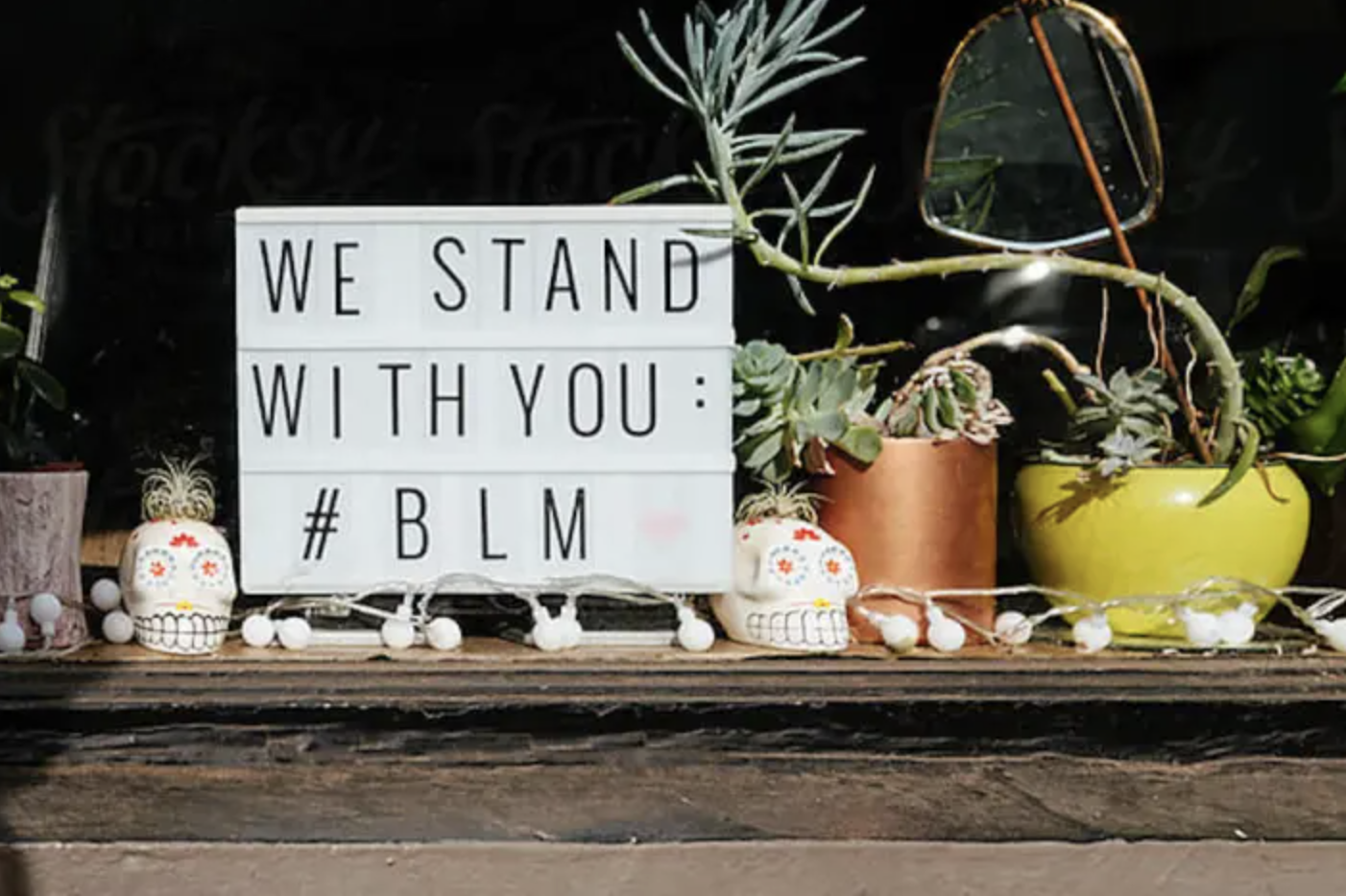 A table with Mexican skull planter pots, string lights, and a sign saying "We stand with you: #BLM".