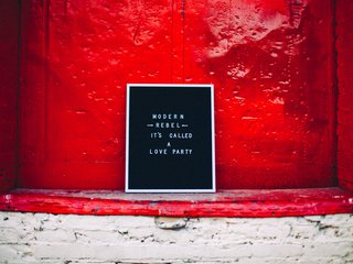 A letter board that reads "Modern Rebel it's called a love party" sits against a red wall