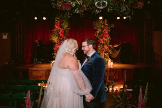 a couple in wedding attire stand in a room holding hands