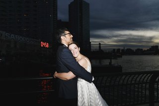 a couple in wedding attire embrace in front of a river at night