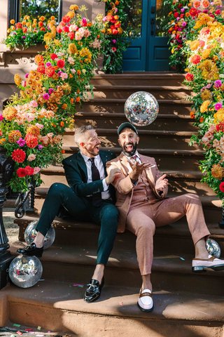 Two white men sit on a building stoop surrounded by disco balls