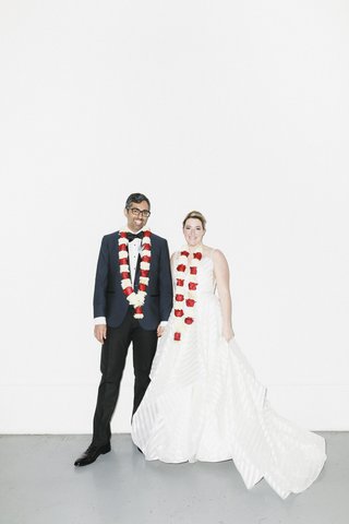A couple in wedding attire stand in front of a white wall