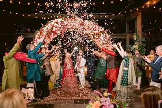 two people stand under a floral arch as petals rain down on them