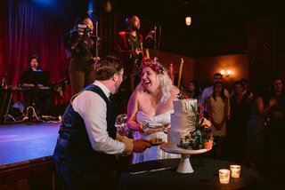 a married couple in wedding attire cut their wedding cake