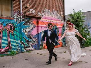 couple in wedding attire holding hands as they walk down a sidewalk with graffitti behind them