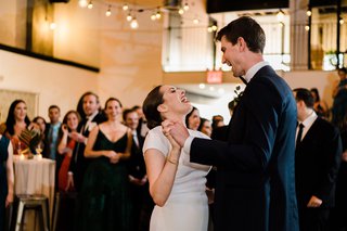 Two people dance and sing together surrounded by loved ones.