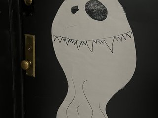 a hand drawn ghost with mismatched eyes is stuck on an apartment front door