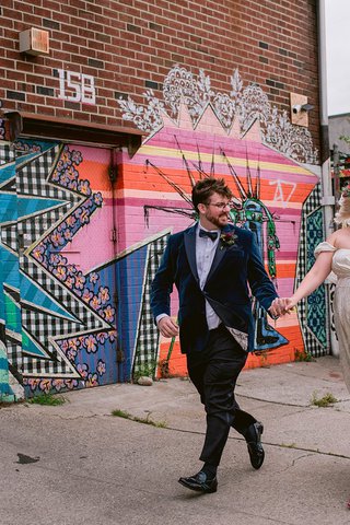 couple in wedding attire holding hands as they walk down a sidewalk with graffitti behind them
