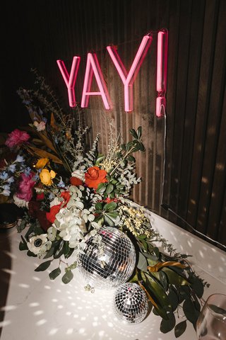 A neon "yay" sign over a disco ball & flowers