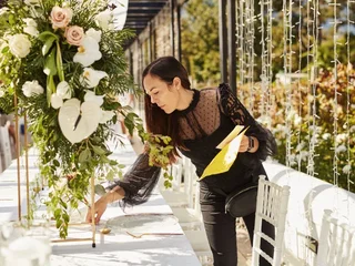 A woman leans over a table at a wedding adjusting the place settings