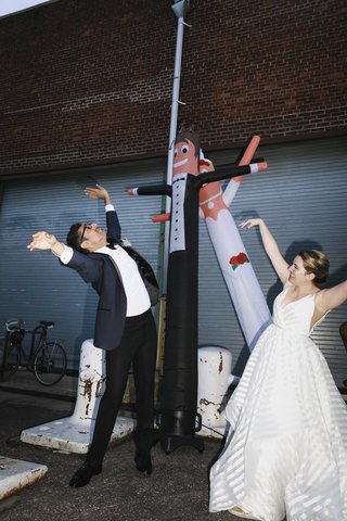 bride and groom throw their hands up in the air next to air dancers