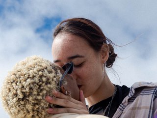 Two people kiss outside with the blue sky behind them