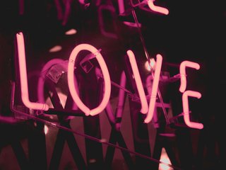 a pink neon sign saying "LOVE" shines in a dark place