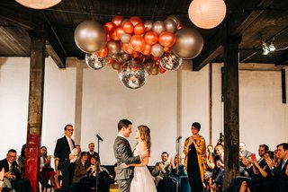 Two people dance underneath balloons and disco balls with their loved ones surrounding them