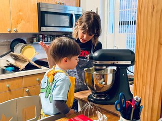 Amy in the kitchen with her son looking at a stand mixer as they make cookies wearing aprons