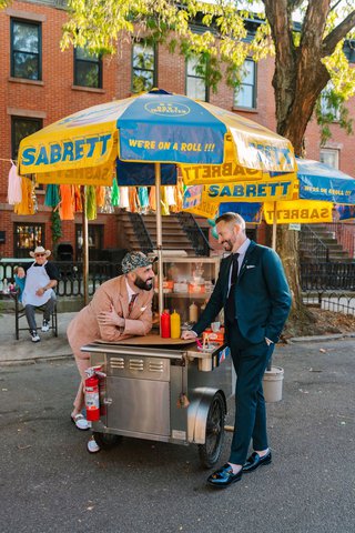 Two white men lean on a hot dog cart