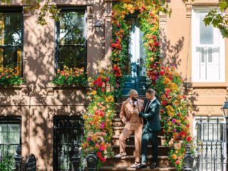 two white men stand lovingly together in front of a brooklyn brownstone building that is decorated with flowers