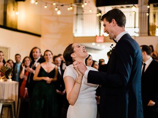 Two people dance and sing together surrounded by loved ones.