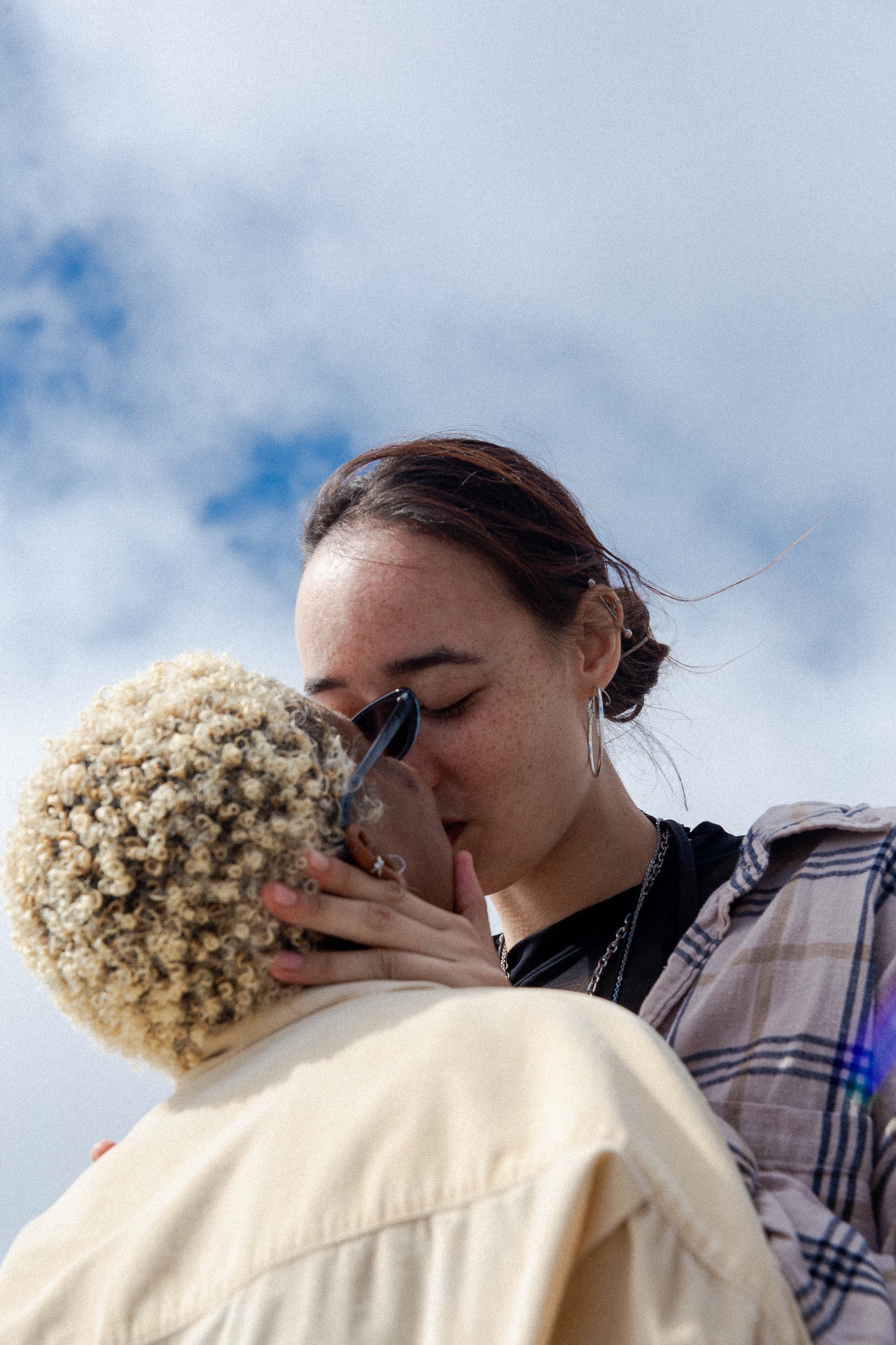 Two people kissing against a blue sky with clouds.