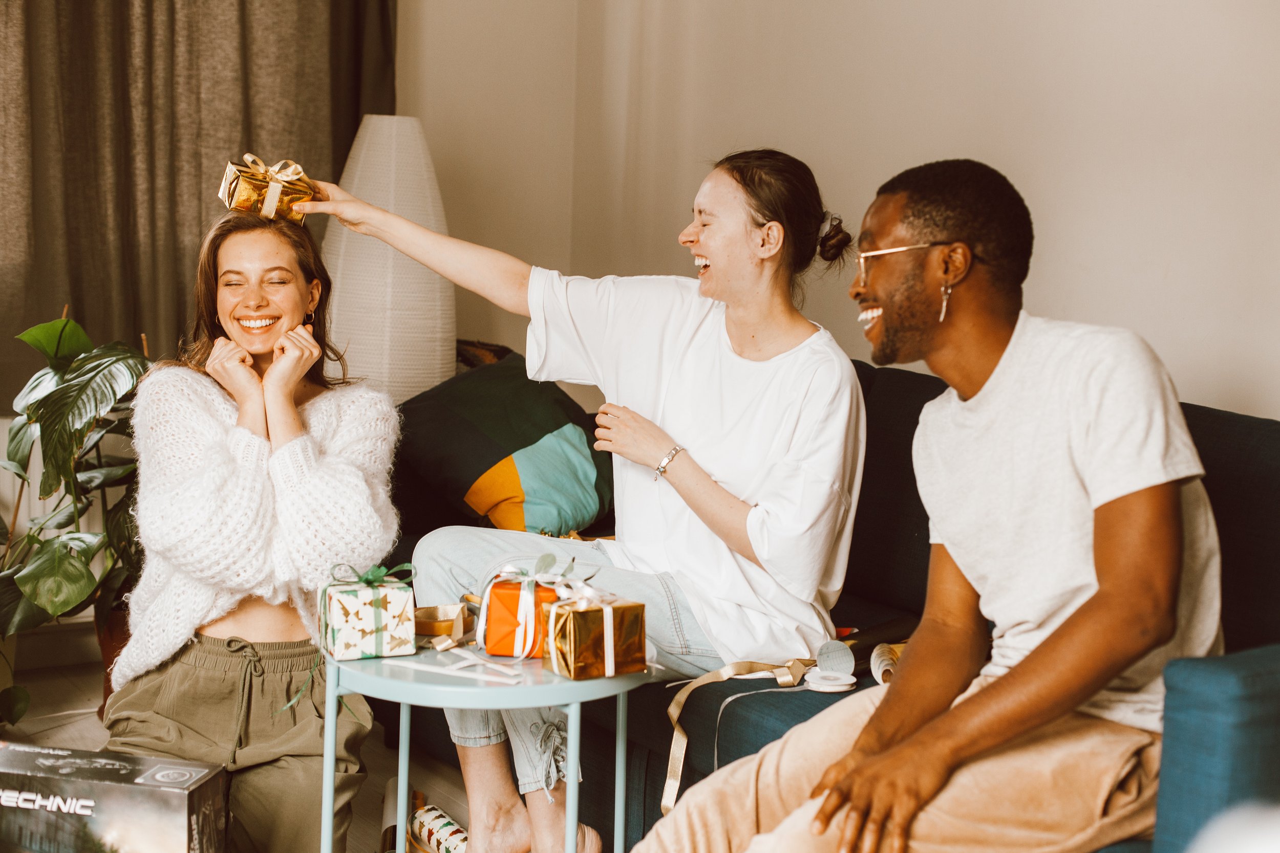 Three people in a room exchanging gifts, laughing.